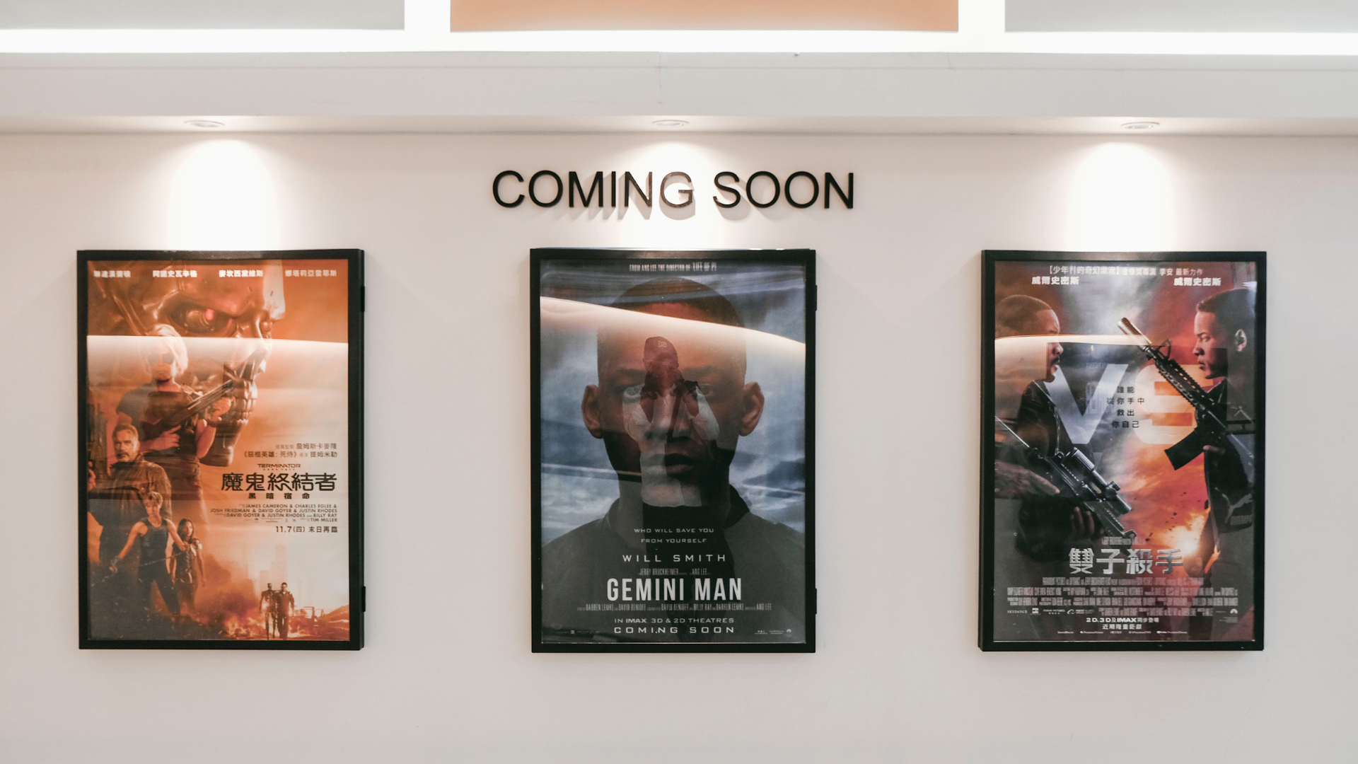 Three framed film posters displayed under a Coming Soon sign in a cinema lobby