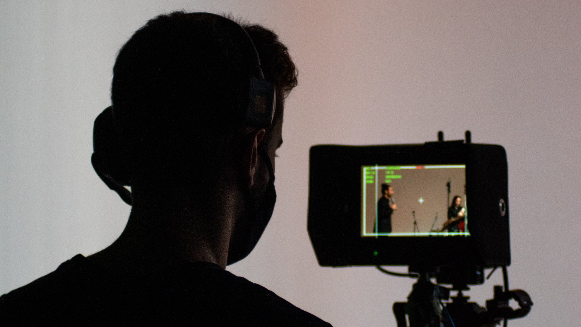 A filmmaker in headphones watches two actors framed on a camera monitor during a shoot